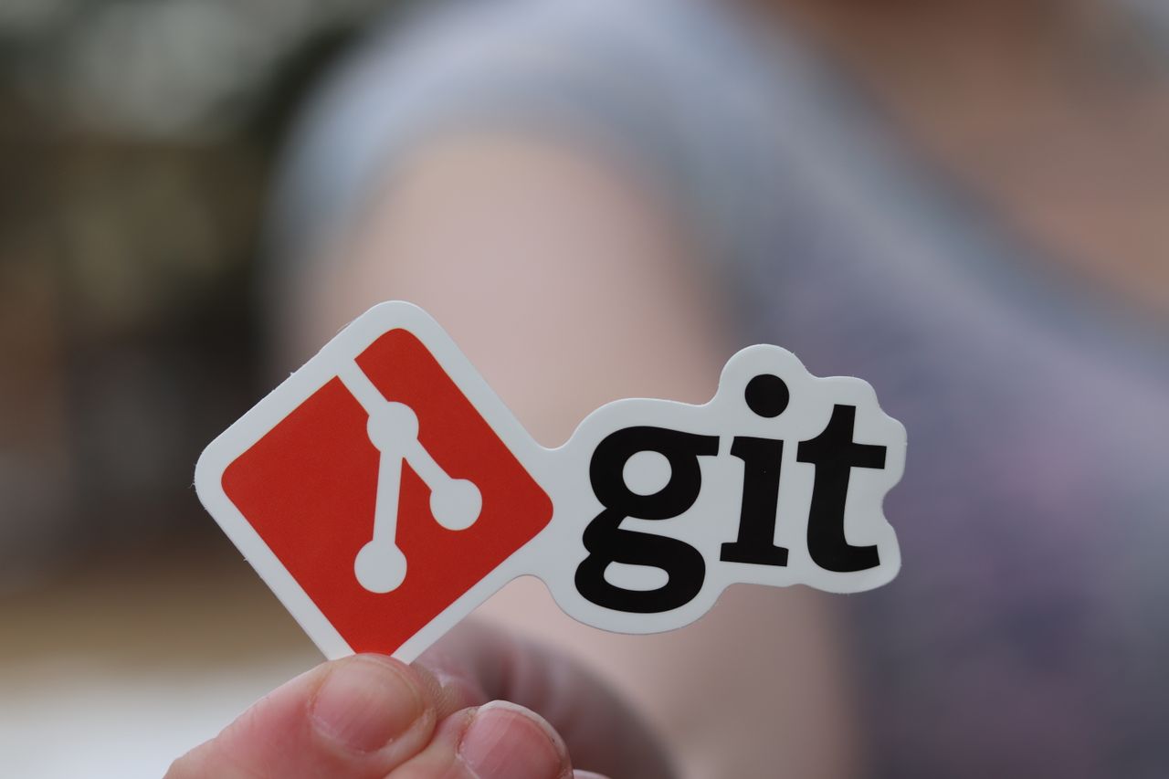 Home Close-up of a person holding a Git sticker, emphasizing software development.